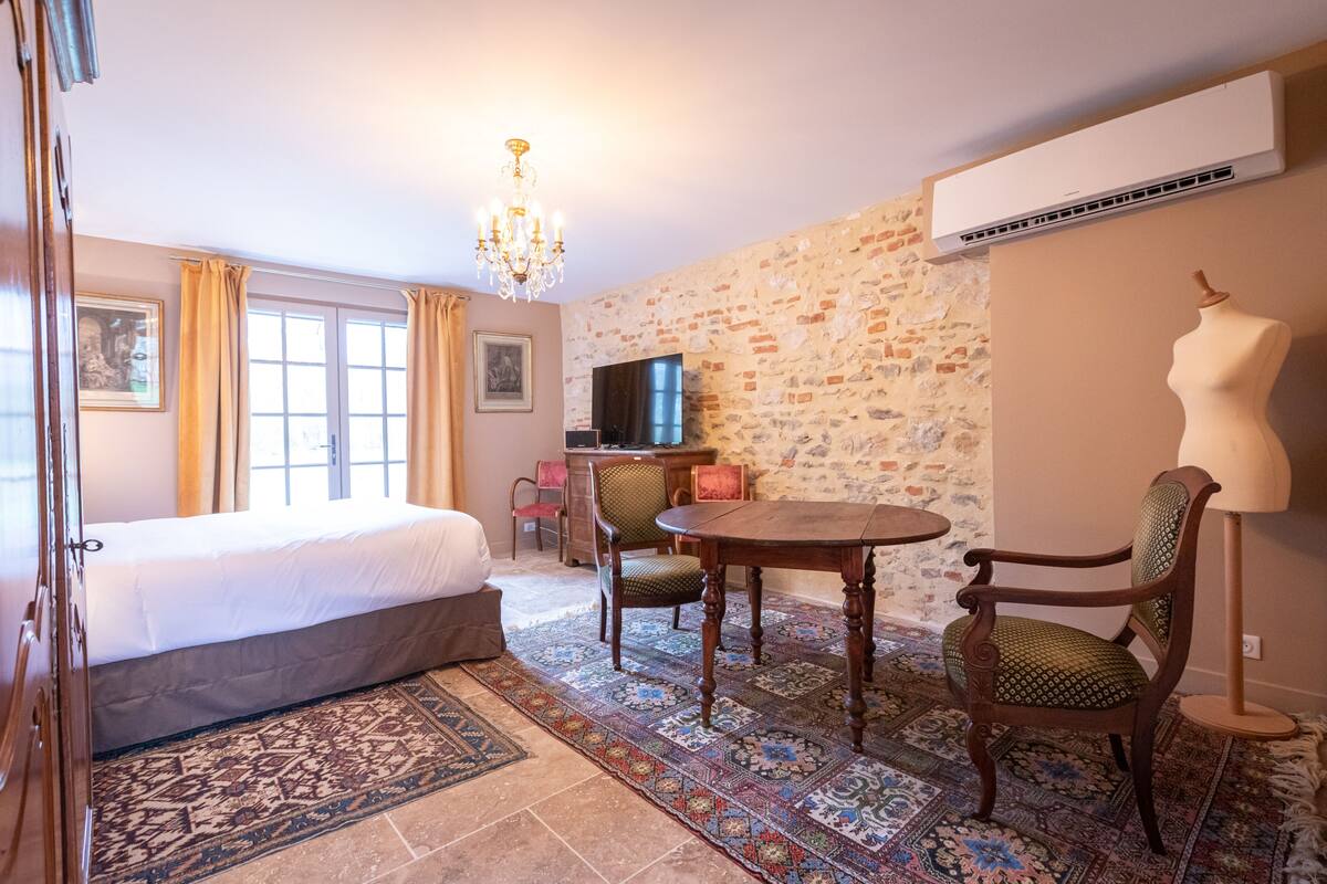 Ein Hotelzimmer mit Bett, Esstisch und Stühlen, einer Kandelaber, einem Fernseher und einer Backsteinwand.