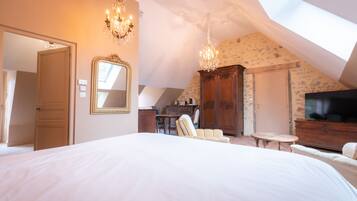 A bedroom with a large bed, a chandelier, a television, and a desk with a chair.