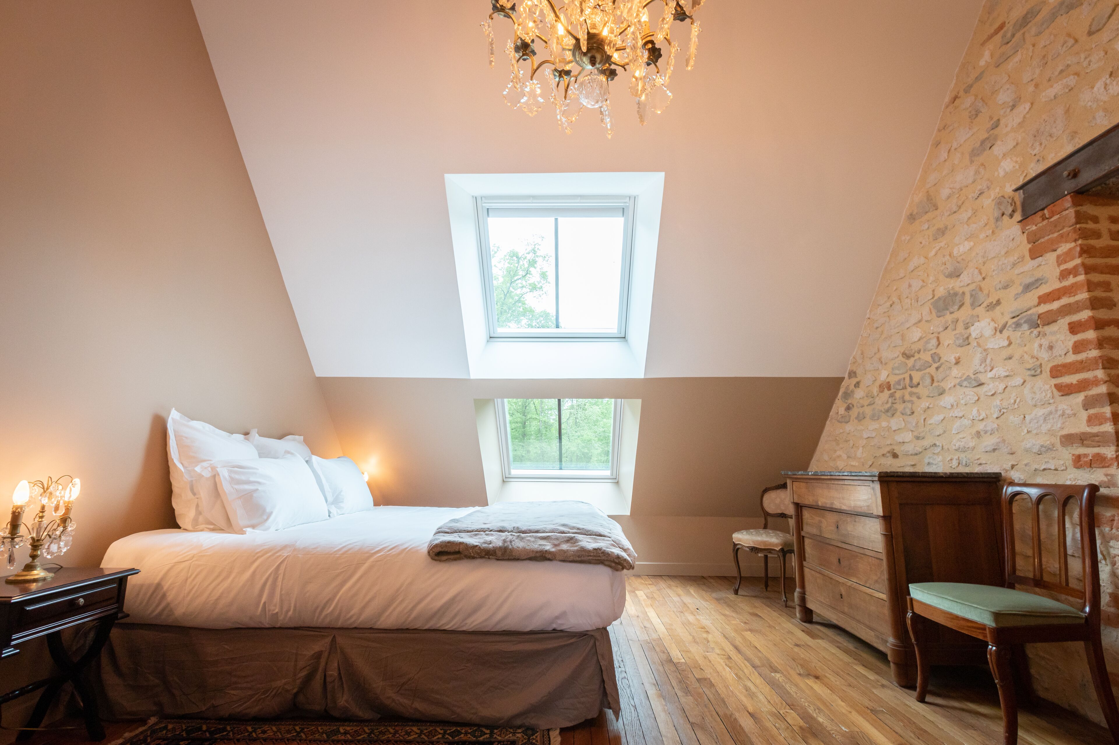 A bedroom with a large bed, a wooden dresser, a chair, and a chandelier.