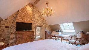 Une chambre avec un mur en pierre, des meubles en bois, un lustre et un téléviseur.