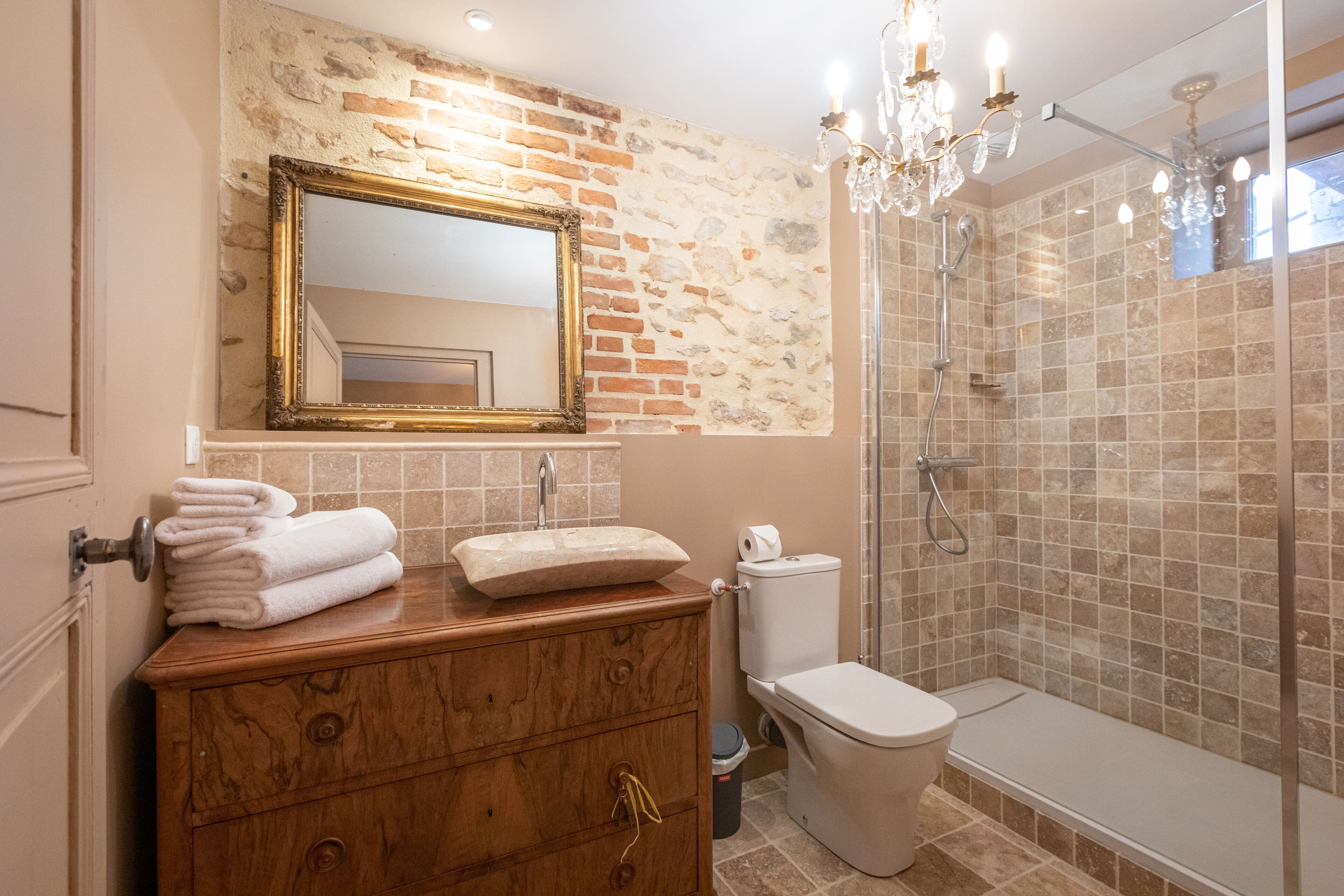 A bathroom with a wooden vanity, a large mirror, a shower enclosure, and a chandelier.
