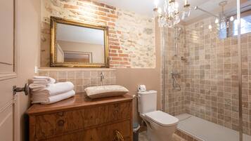 A bathroom with a wooden vanity, a large mirror, a shower enclosure, and a chandelier.
