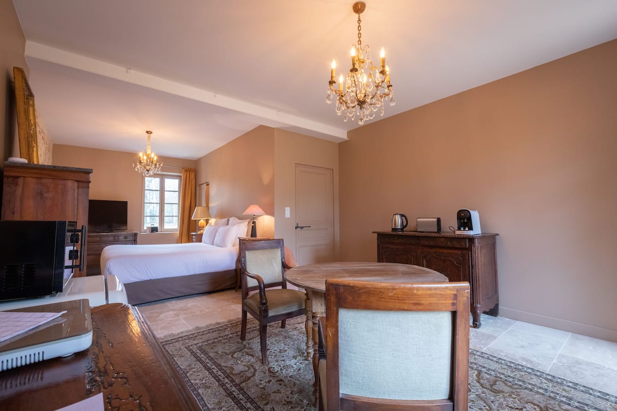 Ein Hotelzimmer mit Bett, Schreibtisch, Stuhl, Fernseher, einer Chandelierleuchte und einem Schminktisch.