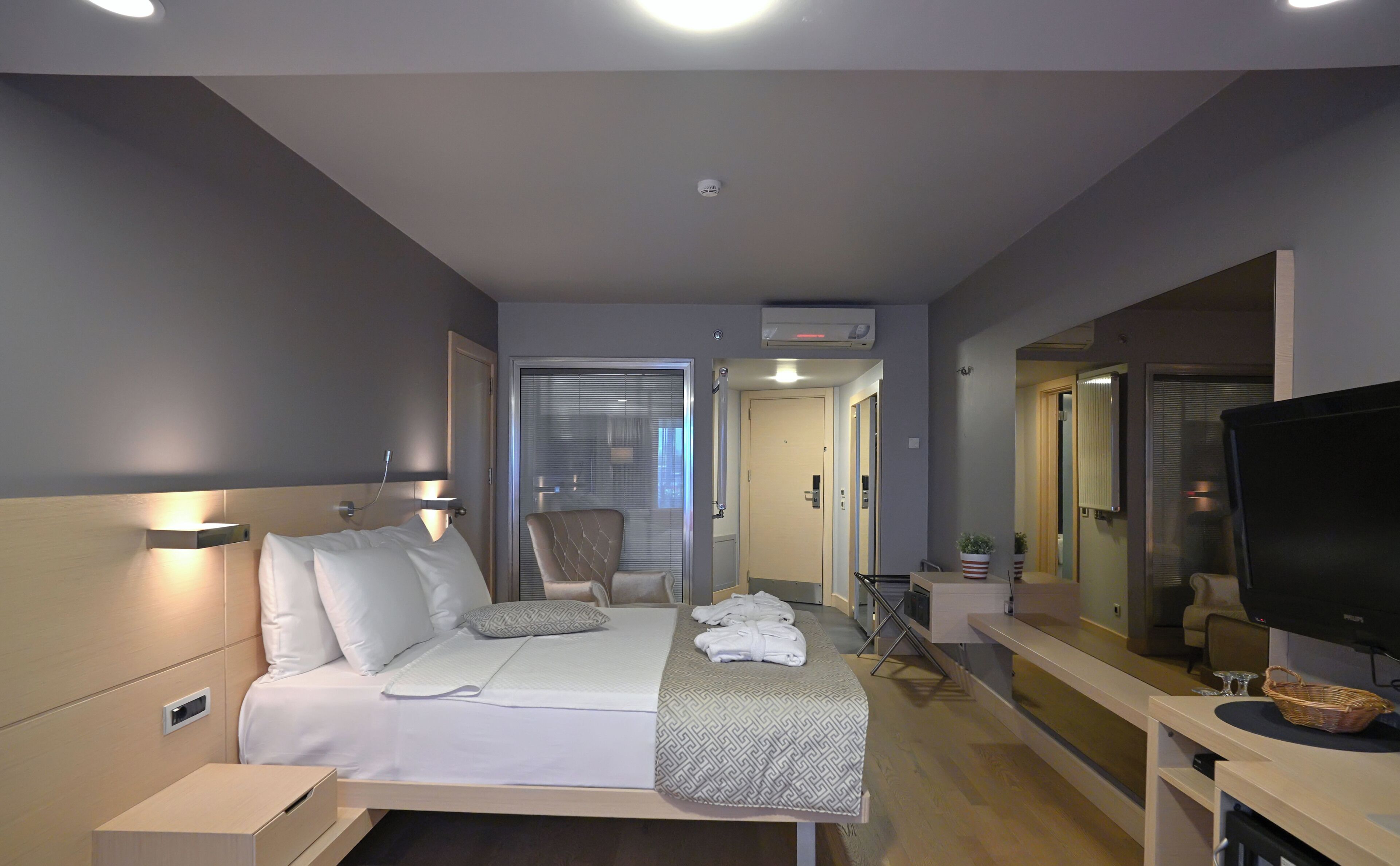 A hotel room with a bed, bedside table, TV, and a mirror.