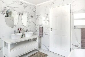 A bathroom with a white marble wall, a white vanity with two sinks, a large mirror, and a door. - 3 Bedroom Hilltop Home With Spectacular Views (Cape Town)