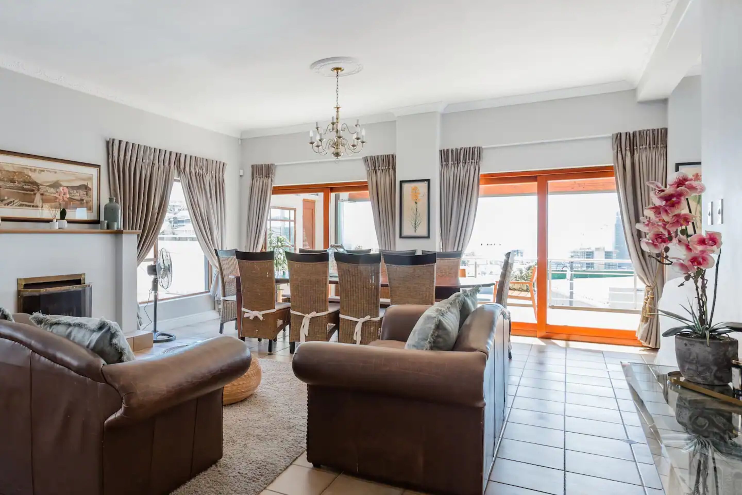 A spacious living room with a brown leather sofa, a small table, and a potted plant.