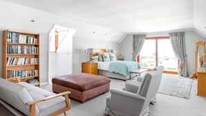 Ein geräumiges Schlafzimmer mit einem großen Bett, einer Sitzecke mit Sofa und Sesseln, einem Bücherregal und Blick durch ein Fenster.