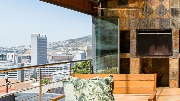 Eine Dachterrasse mit einer Holzbank, einem Tisch und Blick auf die Stadt.