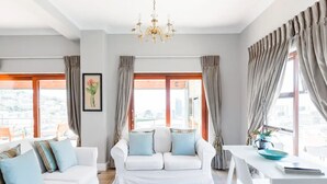 Ein modernes Wohnzimmer mit einem weißen Sofa, einem Esstisch und großen Fenstern mit Vorhängen.