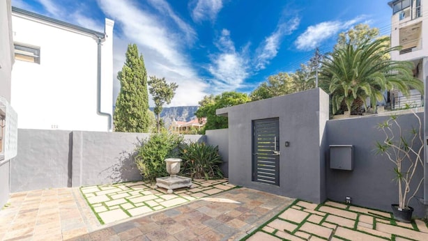 A modern outdoor patio with stone tiles and green grass patterns, a grey wall, and a door with a metal handle. - Spaciaous 2 Bedroom Bokaap Apartment (Cape Town)