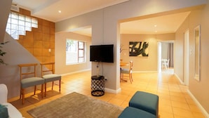 A spacious living area with a staircase, a flat-screen TV mounted on the wall, and a dining area with chairs and a table. - Spaciaous 2 Bedroom Bokaap Apartment (Cape Town)