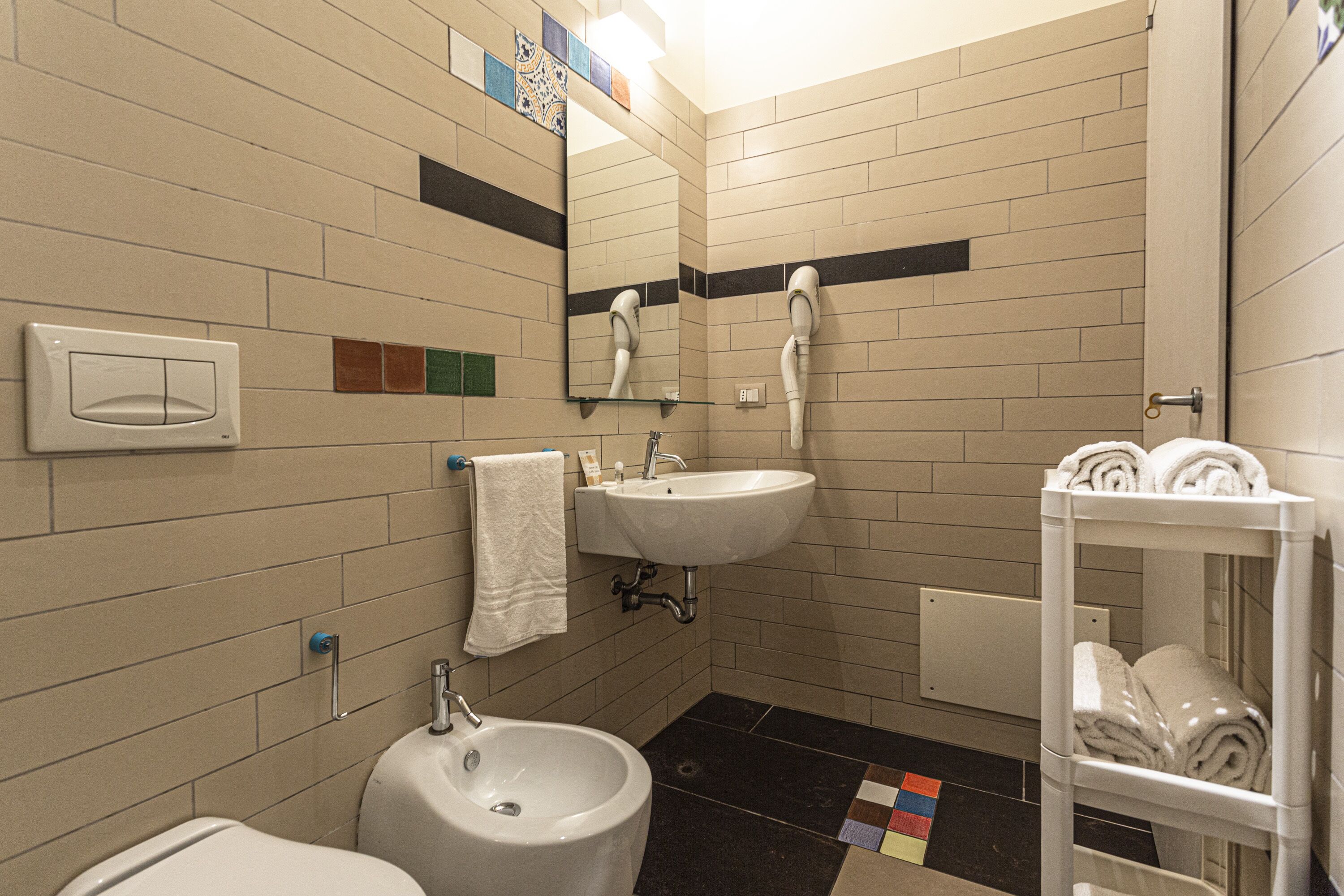 Et badeværelse med vask, spejl, håndklædestativ og toilet.