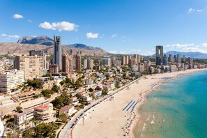 A coastal cityscape with high-rise buildings, a beach, and mountains in the background.
