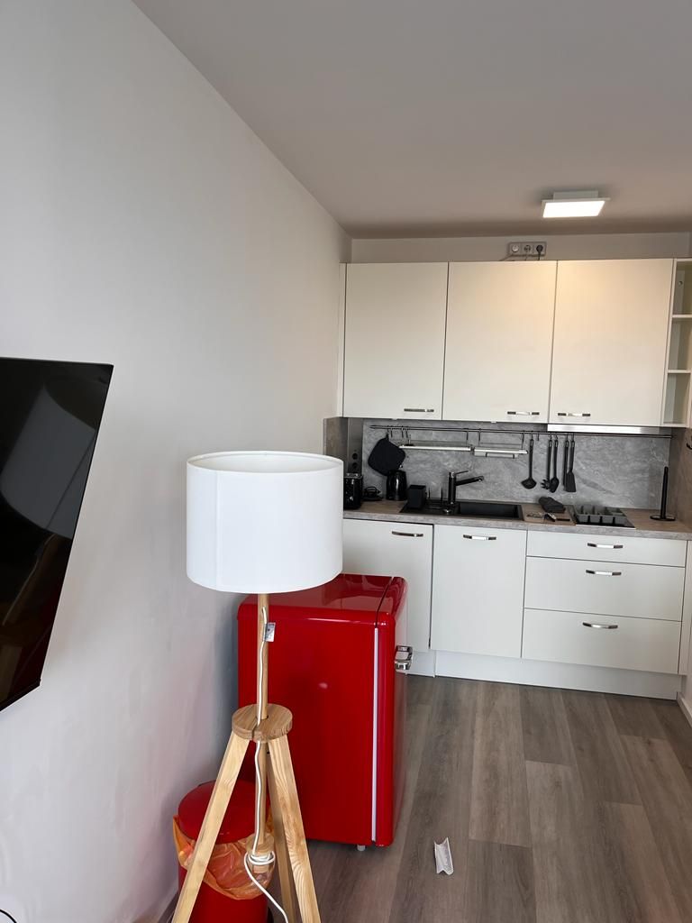 Una cocina moderna con armarios blancos, un electrodoméstico rojo y suelo de madera.