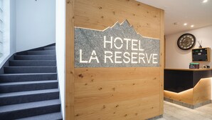 A hotel reception desk with a sign reading "HOTEL LA RESERVE" and a staircase leading to an upper floor. - Hotel La Réserve (St. Niklaus)