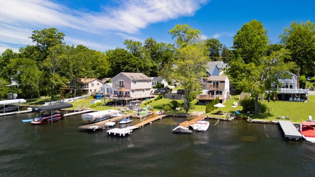 A marina with several boats docked, surrounded by residential houses with large windows and balconies. - Waterfront Cottage at Highland Lake w/dock (Winsted)