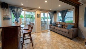 A spacious living area with a wooden bar, a brown leather sofa, and a dining table with chairs. - Waterfront Cottage at Highland Lake w/dock (Winsted)