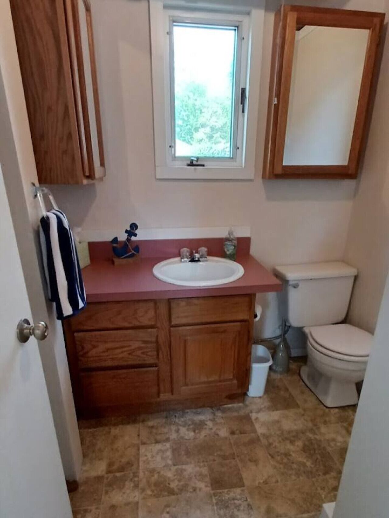 A bathroom with a wooden vanity, a white sink, a toilet, and a window above the sink.