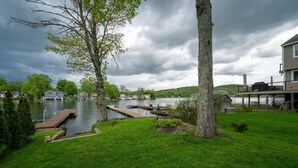 A lakeside property with a dock, grassy lawn, and a house with a deck overlooking the water. - Waterfront Cottage at Highland Lake w/dock (Winsted)