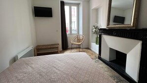 Une chambre à coucher avec un lit, une chaise, une cheminée, un miroir et une fenêtre avec des rideaux.