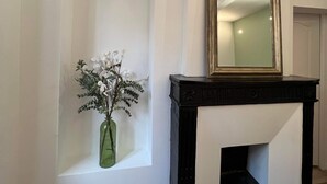 Un couloir avec un mur blanc, une cheminée noire et un vase vert contenant des fleurs.