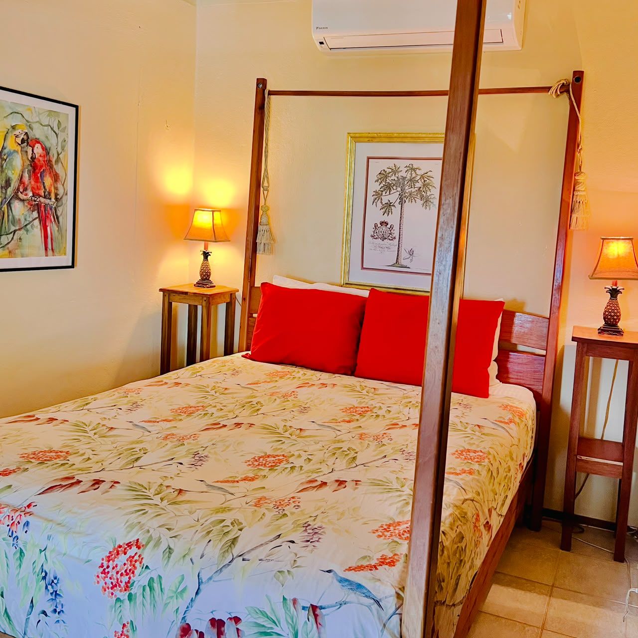 A four-poster bed with a floral bedspread, two bedside tables with lamps, and a framed botanical illustration on the wall.