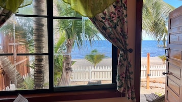 A window with a view of a beach, palm trees, and a wooden fence.