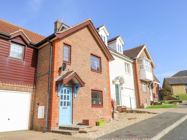 A two-story brick house with a red door and white trim, a garage, and a small garden with gravel and plants. - Tennyson View (Totland Bay)