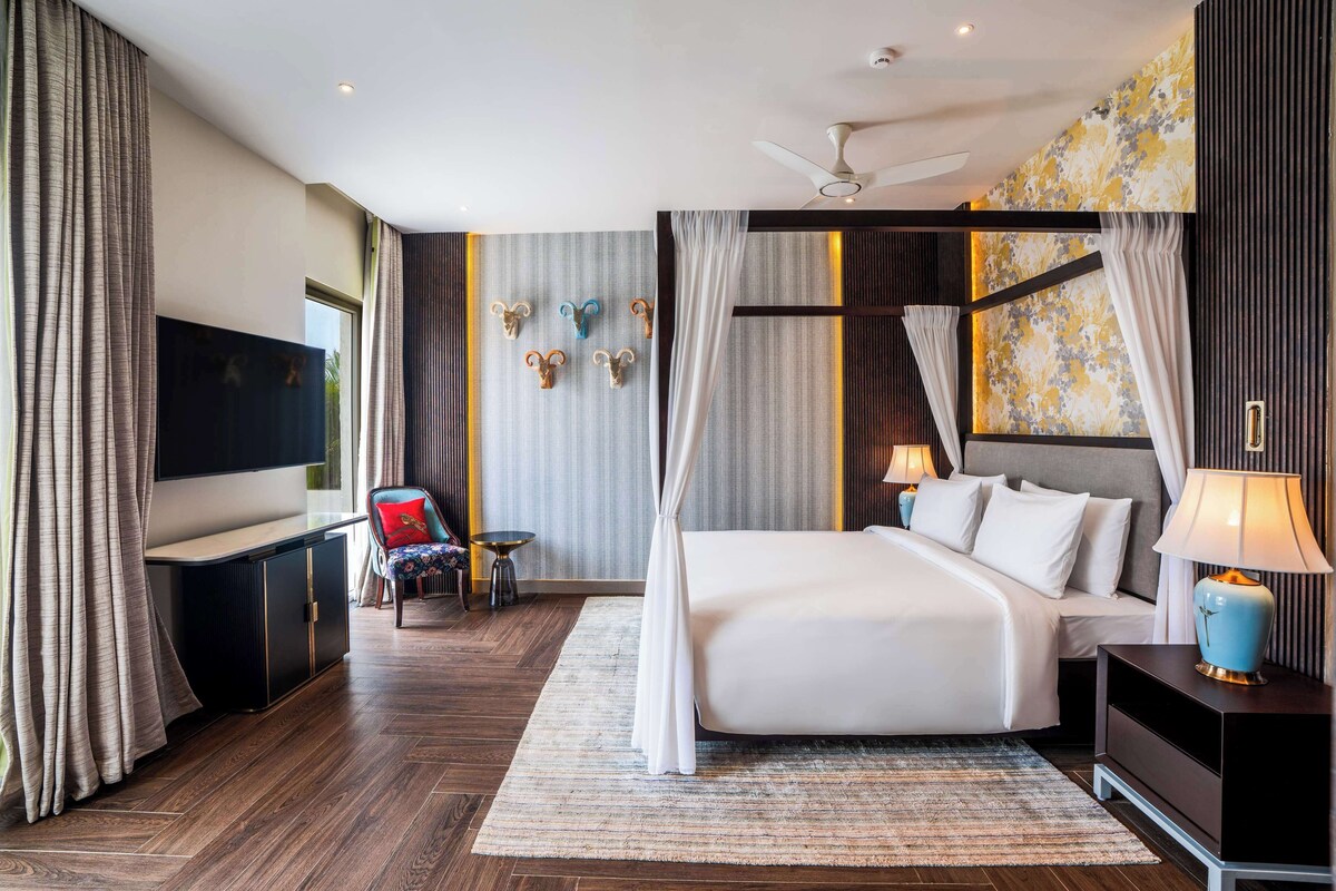 A modern hotel room with a large bed, a flat-screen TV, a ceiling fan, and a decorative wall with animal horns.