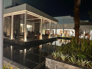 A modern outdoor pool area with a glass-enclosed lounge, surrounded by plants and a stone structure. - Pramod Lands End Resort, a Member of Radisson Individuals (Brahmapur)