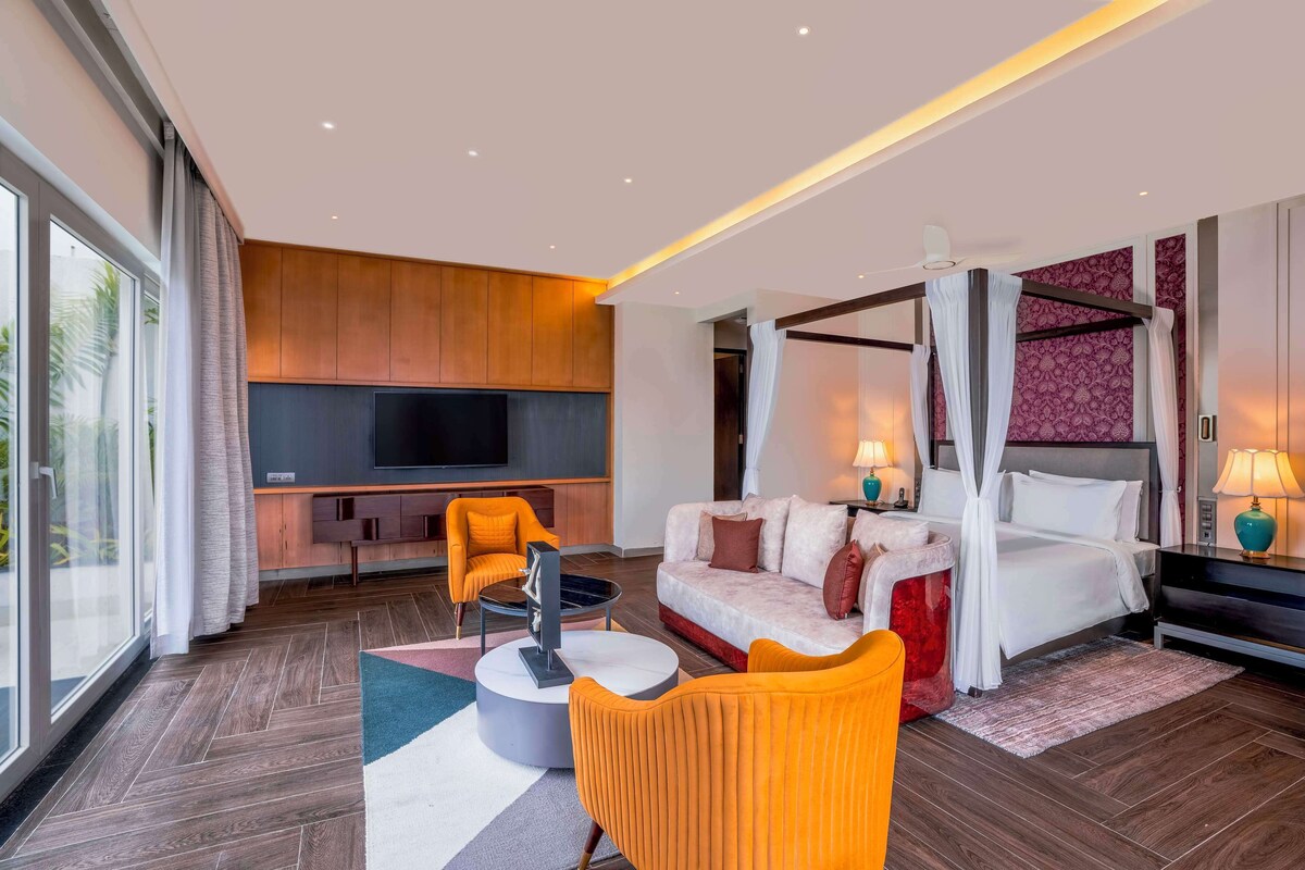 A modern hotel room with a large bed, a sofa, a TV, and a balcony with curtains.