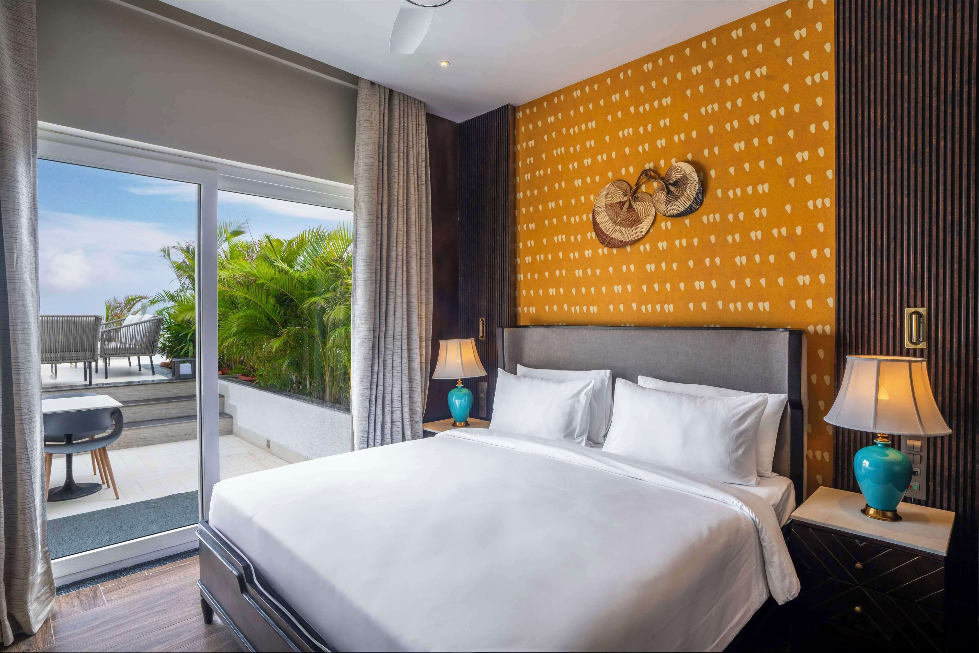 A hotel room with a large bed, two bedside tables with lamps, a view of the outdoors, and a patterned wall.