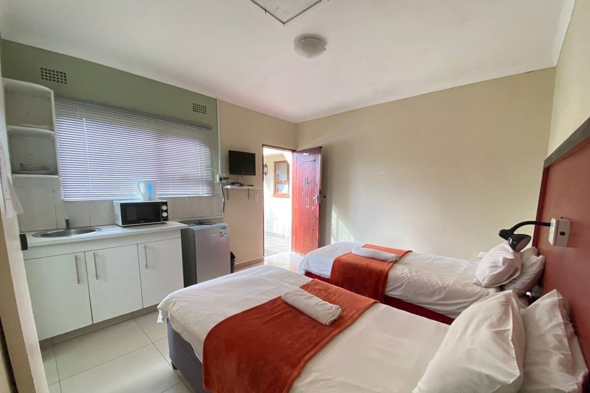 Een hotelkamer met twee bedden, een kitchenette, een televisie en een badkamer zichtbaar door een open deur.