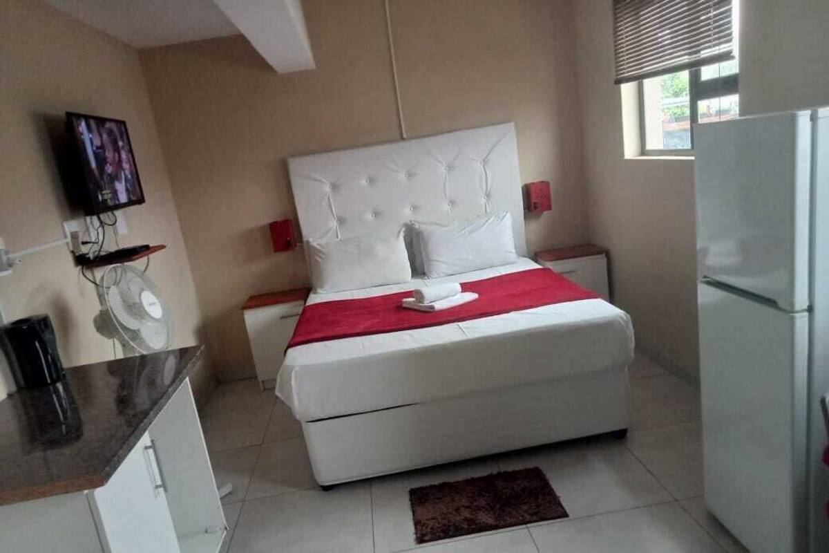 Een slaapkamer met een bed, een televisie, een koelkast en een kleine keukenhoek.