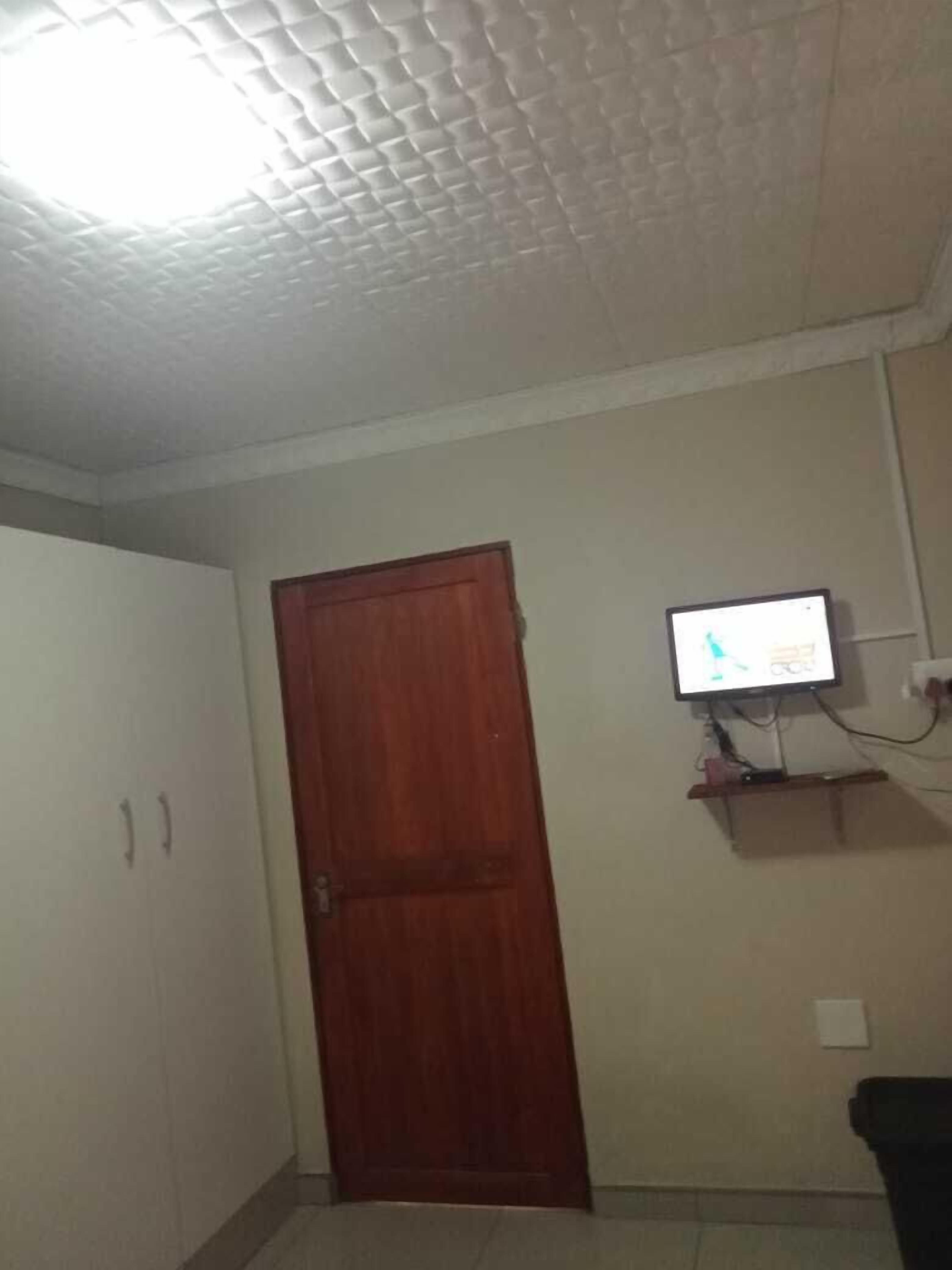 Una habitación con puerta de madera, televisión montada en la pared y techo con textura.