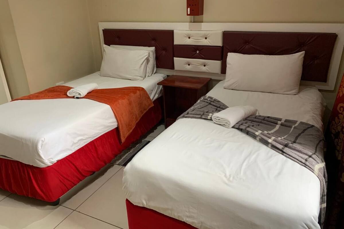 Een hotelkamer met twee bedden, elk voorzien van een rode sprei en witte lakens. Daartussen staat een houten nachtkastje en erboven een rode wandkast.