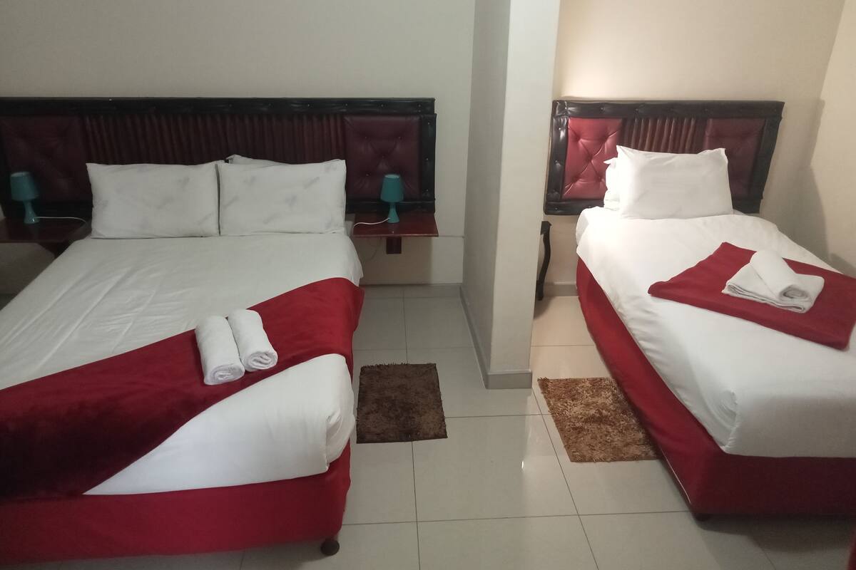 Een hotelkamer met twee bedden, elk voorzien van witte lakens en rode dekens. Er staan twee nachtkastjes met lampen en er ligt een bruin vloerkleed.
