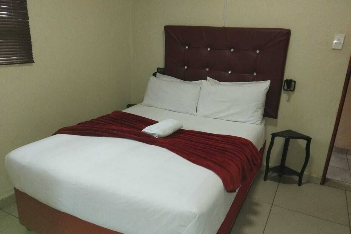 Een standaard hotelkamer met een enkel bed, nachtkastje en een klein krukje.