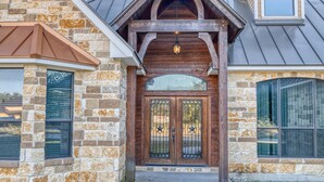A stone facade with a wooden entrance, large windows, and a metal roof. - Tatanka @ Frio Premier Rental Homes (Concan)