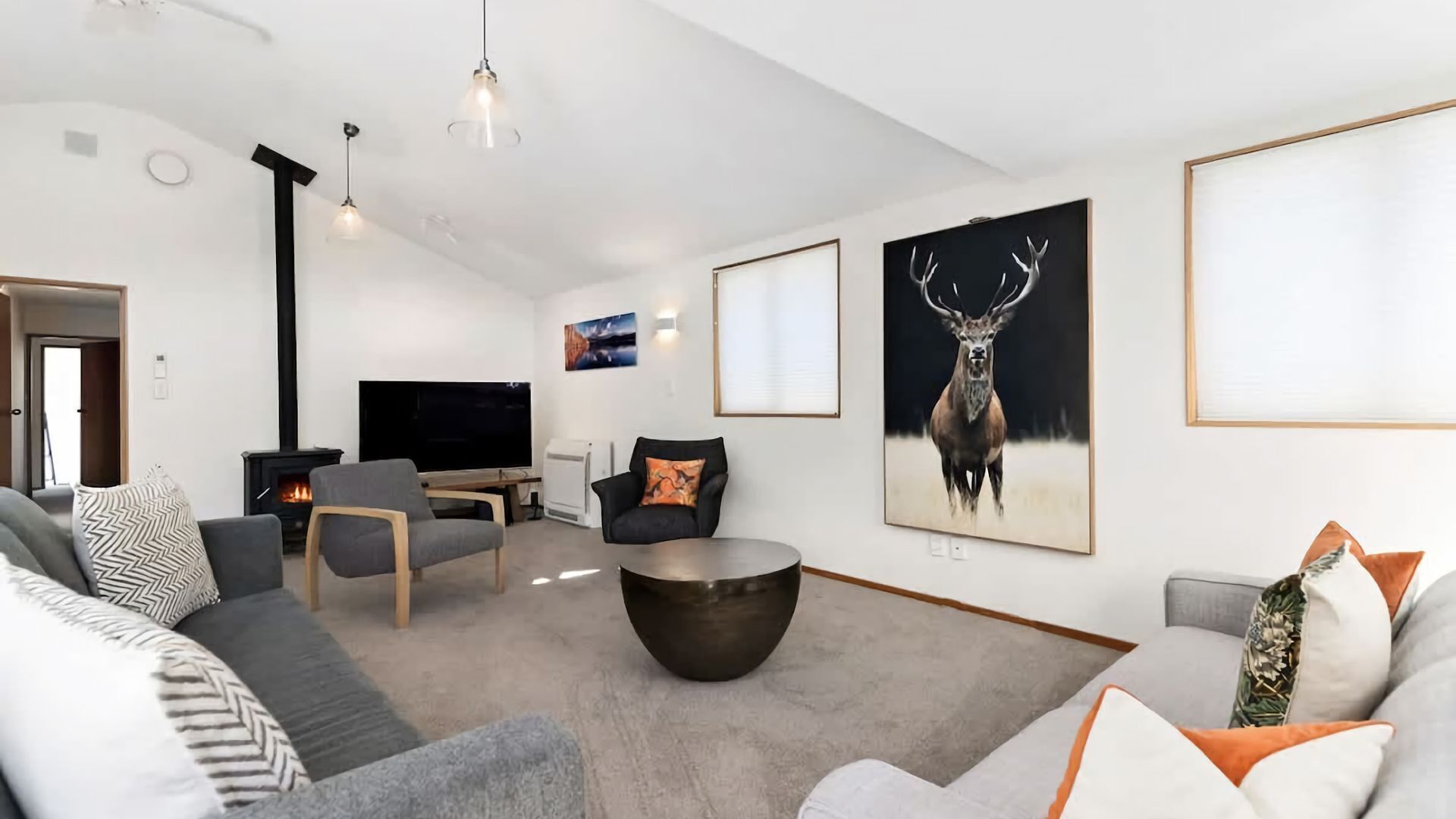 A modern living room with a fireplace, a flat-screen TV, and a large deer painting.