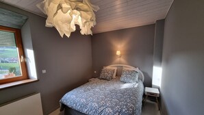 Un dormitori amb un llit, una làmpada penjada a la paret i una finestra amb persianes.