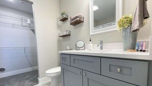 A bathroom with a grey vanity, a toilet, a shower, and a mirror. - Main Floor Cozy 2 Bedroom Condo with a master suite in Bettendorf (Bettendorf)