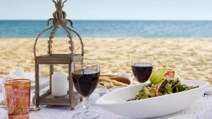 A table set on a beach with a candle, wine glasses, and a bowl of salad. - Fedora Hotel (Rimini)