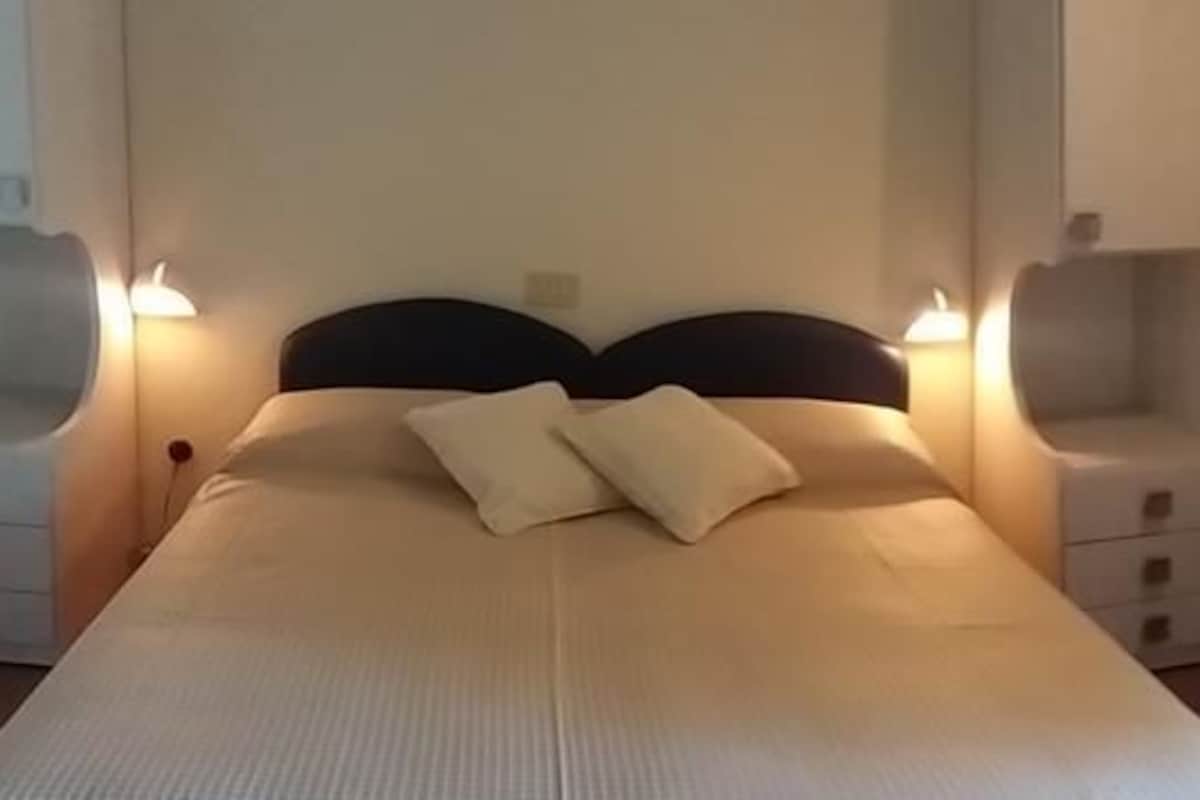 A neatly made bed with two pillows, bedside tables with lamps, and a small shelf unit.