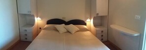 A neatly made bed with two pillows, bedside tables with lamps, and a small shelf unit. - Fedora Hotel (Rimini)