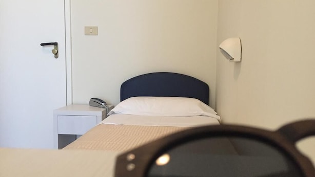 A single bed with a headboard, a bedside table with a lamp, and a door with a lock. - Fedora Hotel (Rimini)