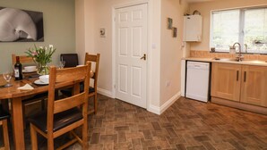 A dining area with a wooden table and chairs, a vase of flowers, and a wine bottle. - Chandler's View (Whitby)