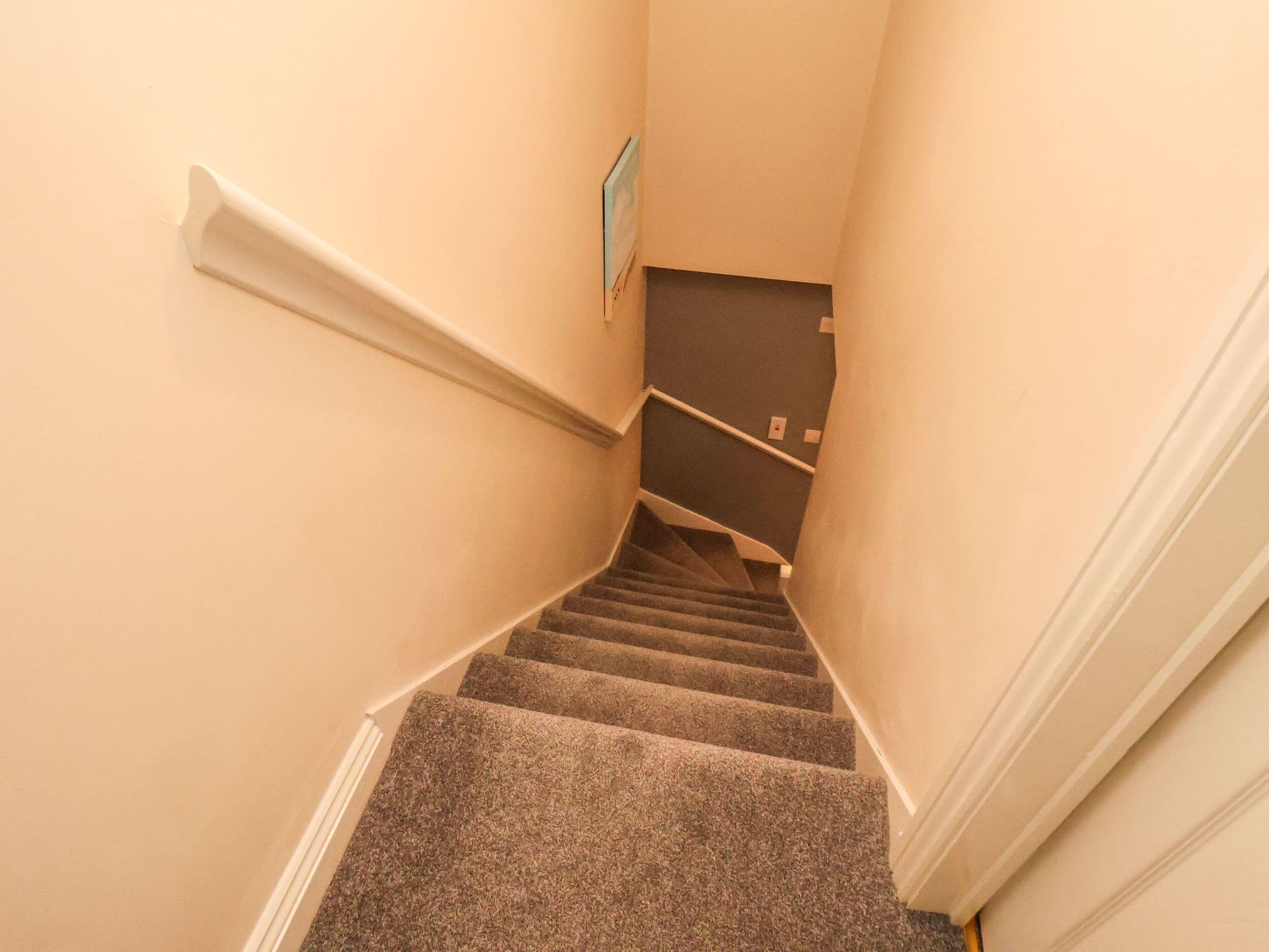 Escada revestida com carpete, com corrimão à esquerda e uma porta na base.