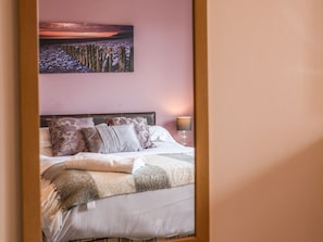 Ein Schlafzimmer mit Bett, Kissen, Decke, Nachttisch, Lampe und einem Landschaftsbild an der Wand.