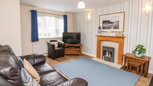 A living room with a leather sofa, a television, a fireplace, and striped wallpaper. - Chandler's View (Whitby)